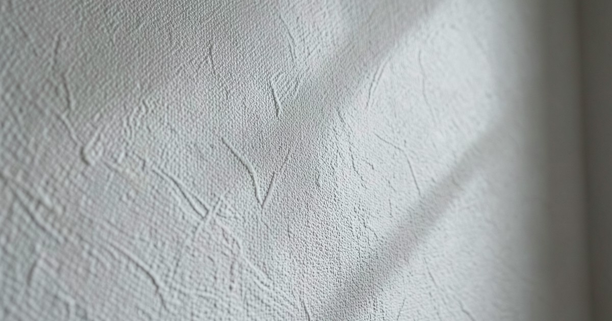 布のような質感の壁紙が貼られた落ち着いた雰囲気の部屋の壁面。